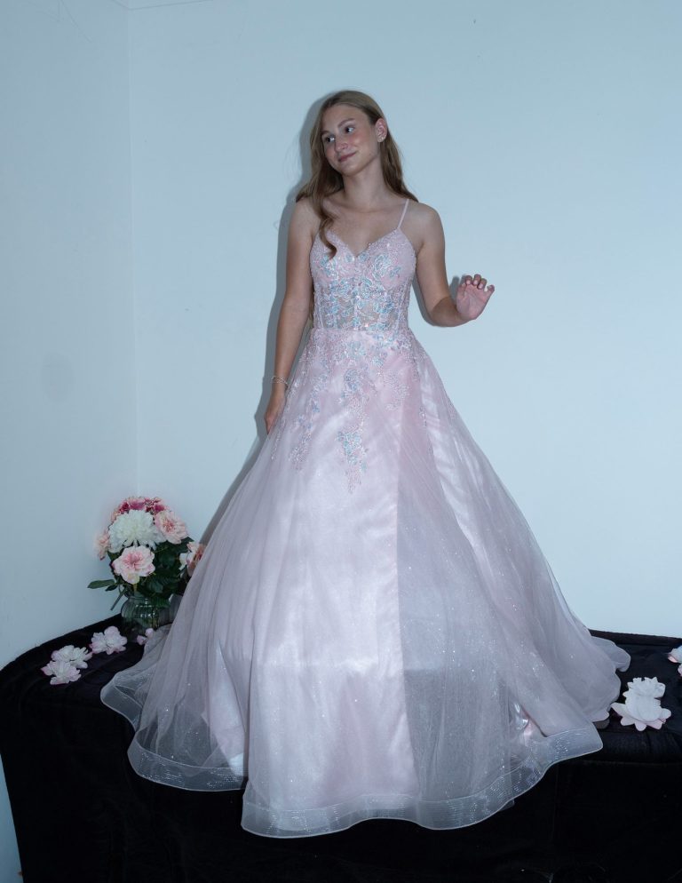 A girl in a pink gown stands on a table, surrounded by floral decorations.