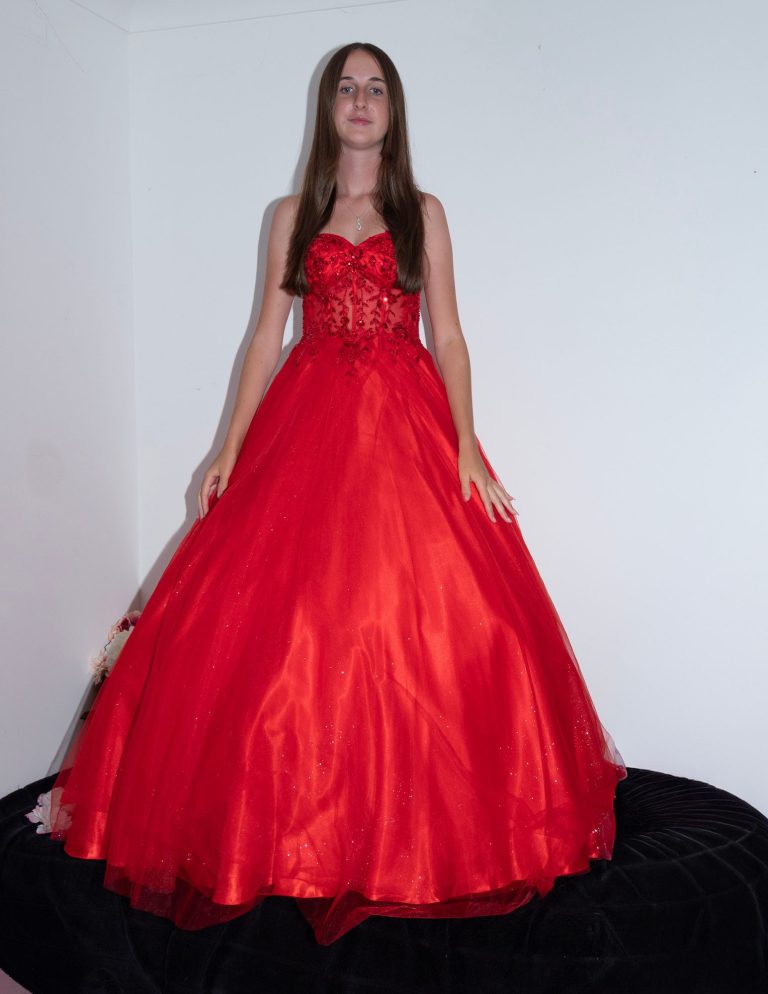 A person wearing a long, flowing red dress, standing against a white wall.