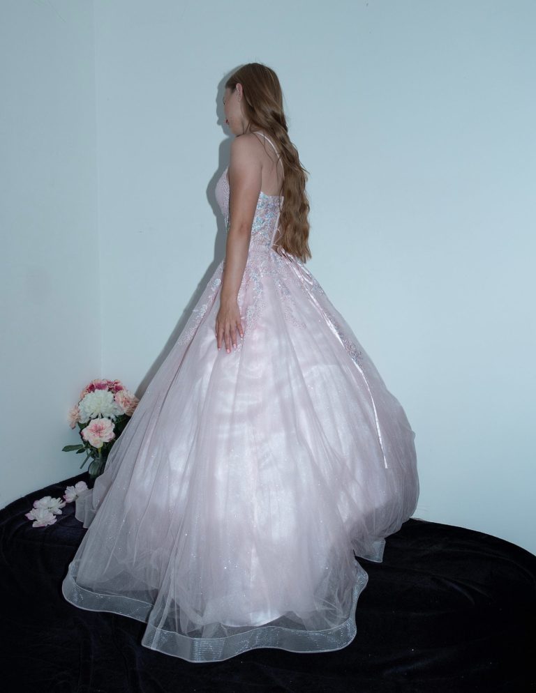A person in a pink ball gown stands gracefully, with a bouquet nearby.