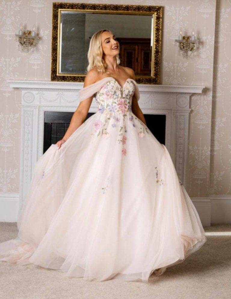 A woman in a pink, floral-embroidered ball gown poses elegantly.