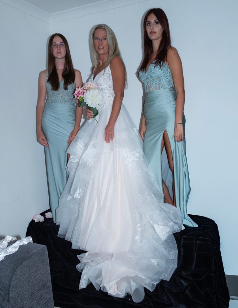 Three women pose together, one in a wedding dress and two in matching gowns.