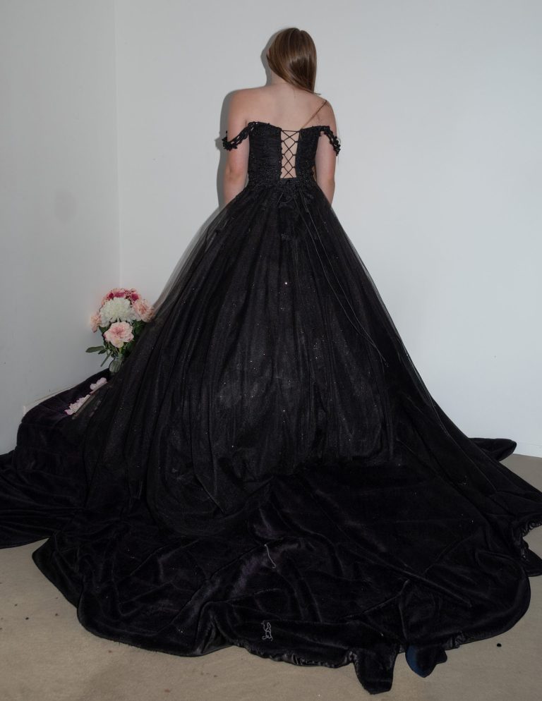 A person in a black off-shoulder gown, viewed from the back, with a long train.