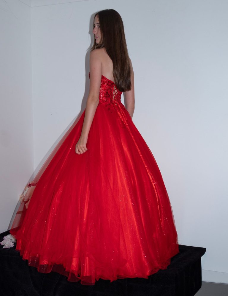 A young woman in a strapless red ball gown, viewed from the back.