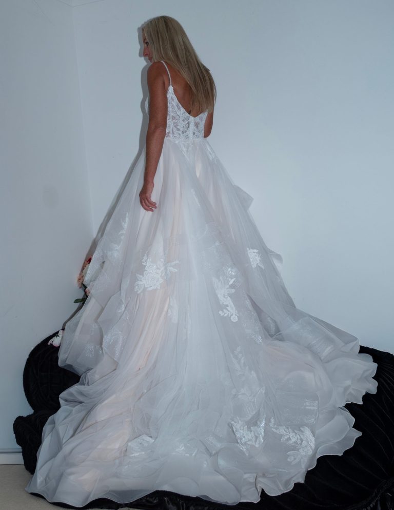A woman in a flowing white wedding dress, standing with her back to the viewer.