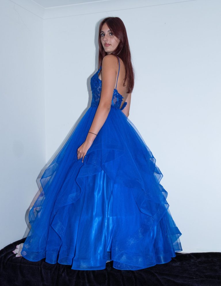 A woman in a blue ball gown with layered tulle, posing with her back to the viewer.