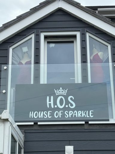 Sign for "House of Sparkle" displayed on a building with red dresses in the windows.